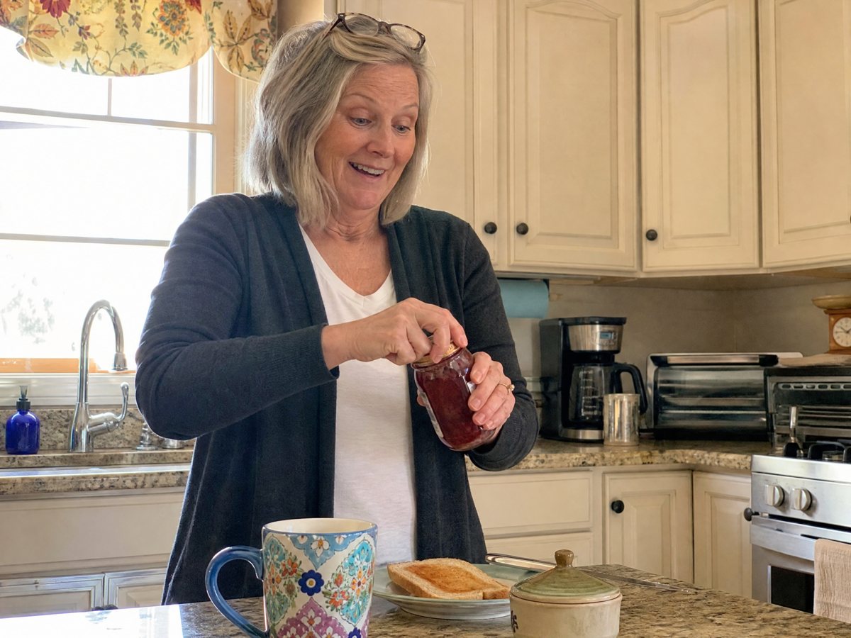 Woman in her kitchen opening a jar of jam with her bare hands